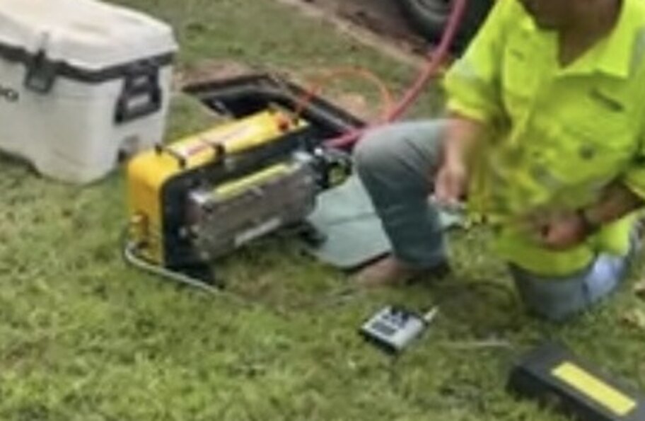 Fiber blowing machine, control unit and air lines set up beside an open hand hole in the field